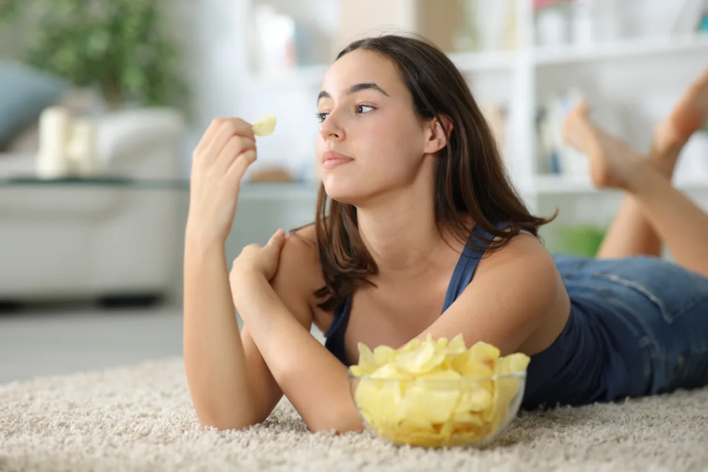 Pensive woman looking away eating potato chips