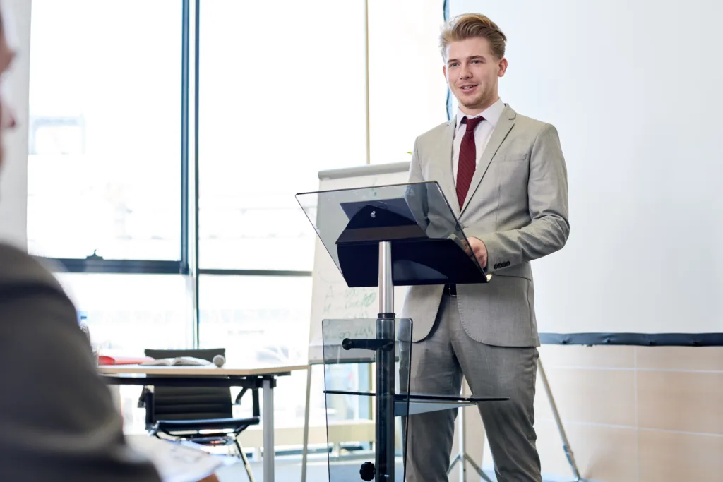 Portrait of smiling young businessman standing by podium while giving speech at conference, copy space