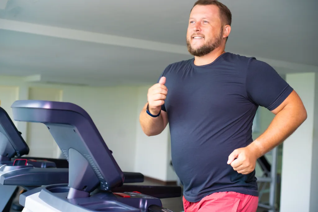 smiling full male runs on a treadmill in a gym. concept of weight loss and sport. side view