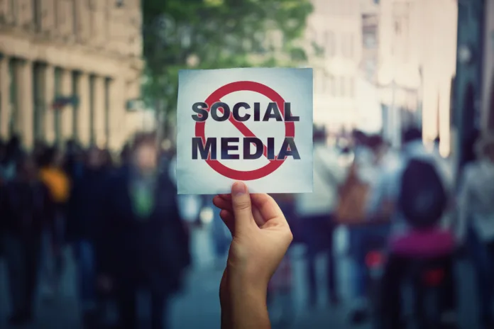 Social media censorship, political war between US president banning social networks. Hand holding a banner with forbidden sign over a crowded street background. Internet communication risk concept.