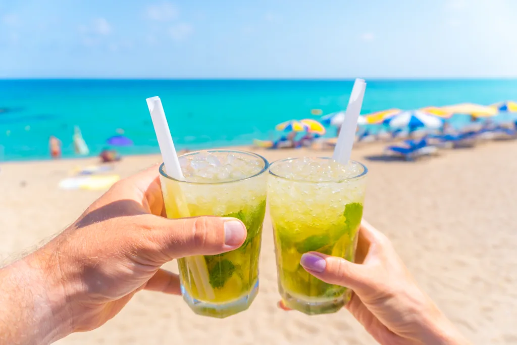 Two hands (male and female) toasting with mojito cocktails on the beach - POV horizontal image of clinking glasses