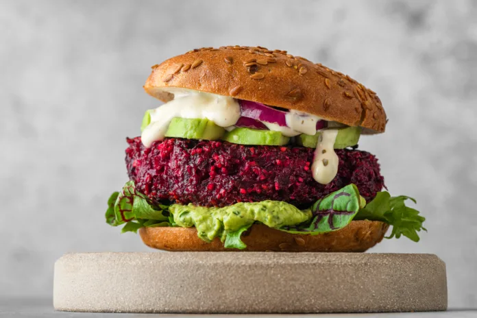 Vegan burger with beetroot cutlet, avocado and vegan mayo sauce on gray background. Healthy veggie food. Close up