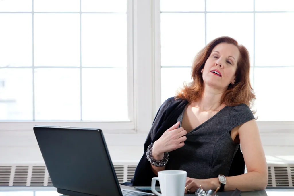 A menopausal woman having a hot flash at her desk in an office.