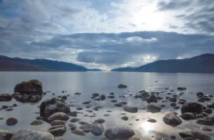 A view across Loch Ness looking down the length of the lake with rocks inn the foreground and dark clouds above, in Scotland, UK