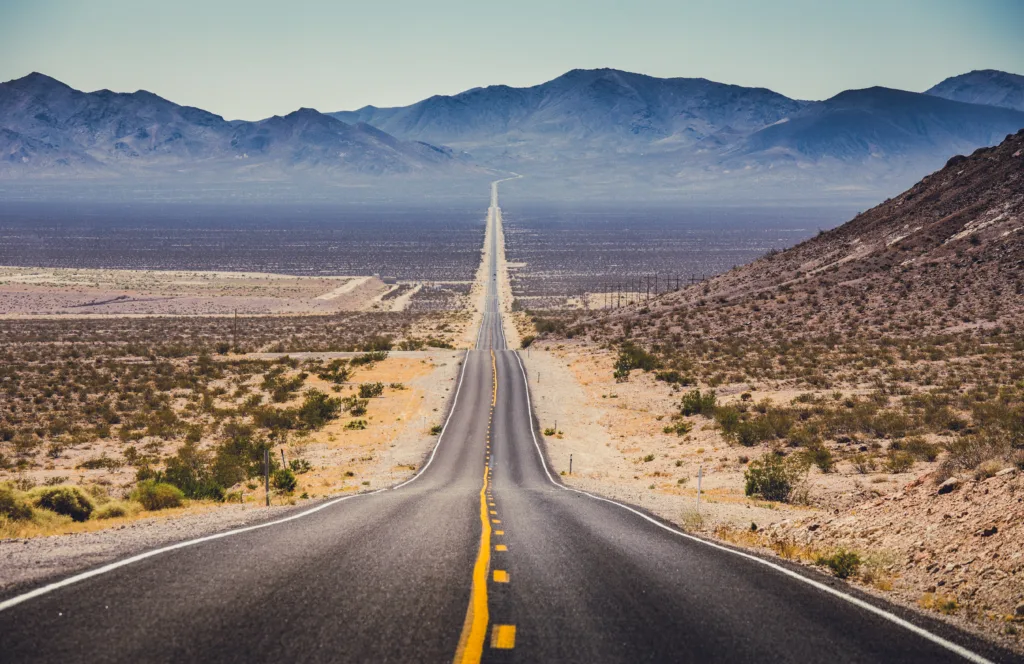 Classic panorama view of an endless straight road running through the barren scenery of the American Southwest with extreme heat haze on a beautiful hot sunny day with blue sky in summer