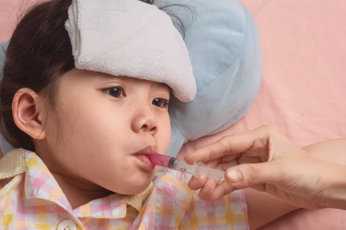 Close up Cute Little Asian Girl Take antipyretic drug paracetamol To reduce headaches From the flu that is epidemic in children on Pink Bed. with Space for your text.