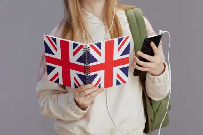 Closeup on girl with backpack, english flag workbook, headphones and smartphone against grey.