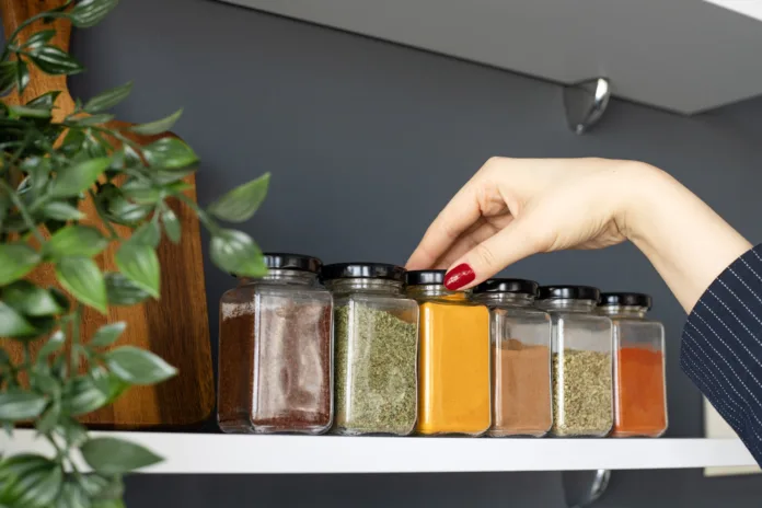 Cropped hand holding jar of spices on kitchen.