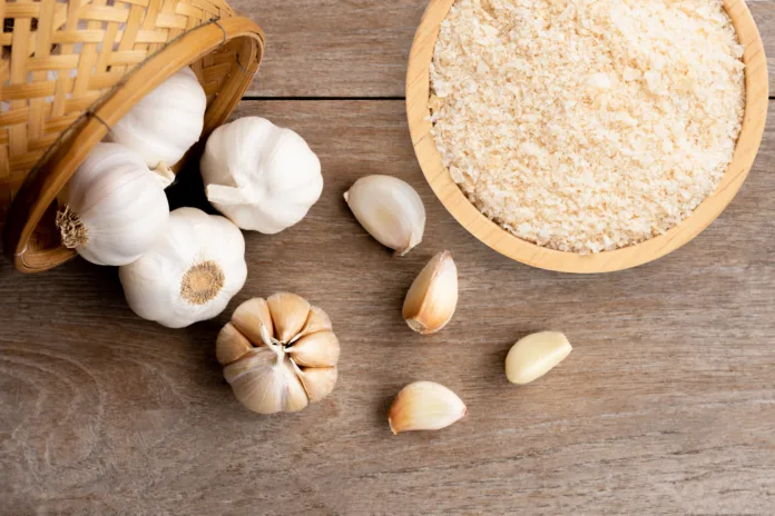 Garlic powder in wooden bowl and bulb of garlic isolated on wooden table background. Top view. Flat lay.