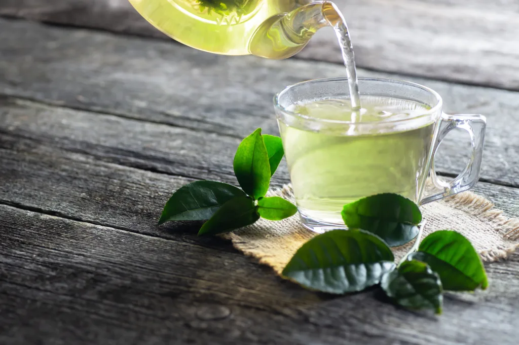 Glass cup of green tea with fresh tea leaves on wooden table, hot drink concept