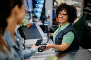 Happy supermarket cashier accepting mobile payment from a customer at store checkout.