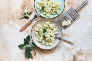 Italian homemade gnocchi with butter, cheese and sage served in two plates on a light marble table. Italian food. Copy space. Flat lay