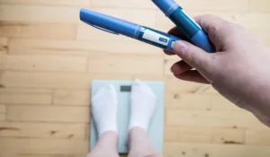 Ozempic Insulin injection pen for diabetics and weight loss. Woman weighs herself and holds Ozempic in her hand. Weight loss concept.