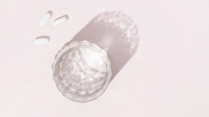 Pills and glass of water on a pink background. Preparations for the treatment of colds, vitamins, wellness complex