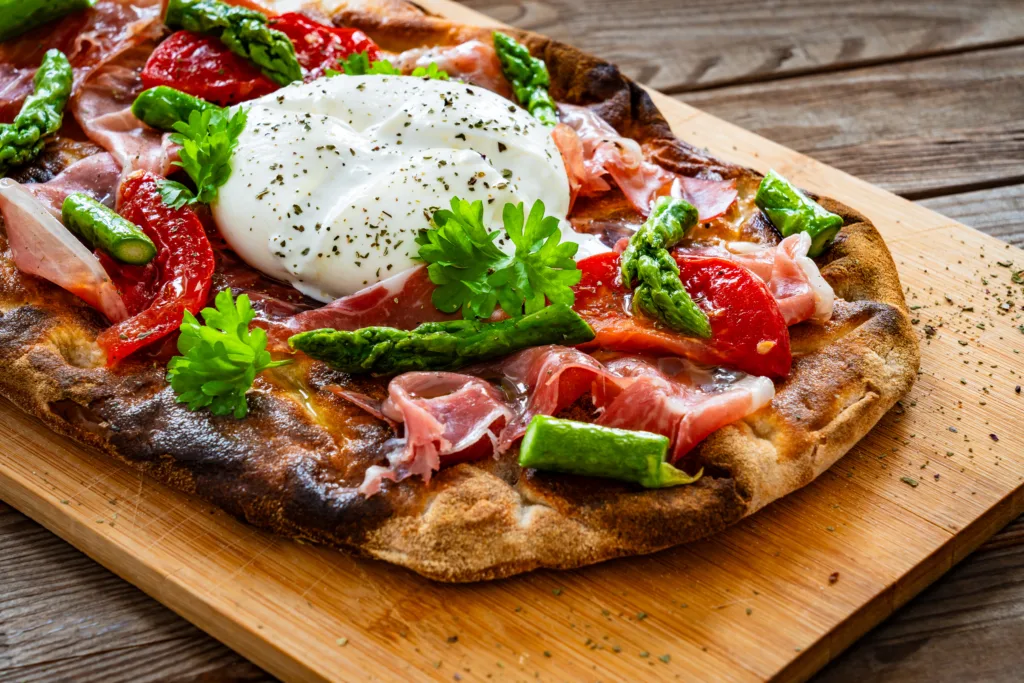 Pinsa - Roman pizza with burrata cheese, ripened ham and green asparagus on wooden background