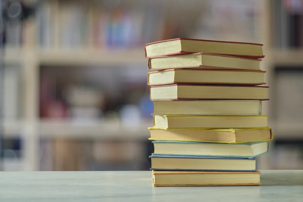 Stack of books with blurred bookshelf background, reading, learning, education or home office concept