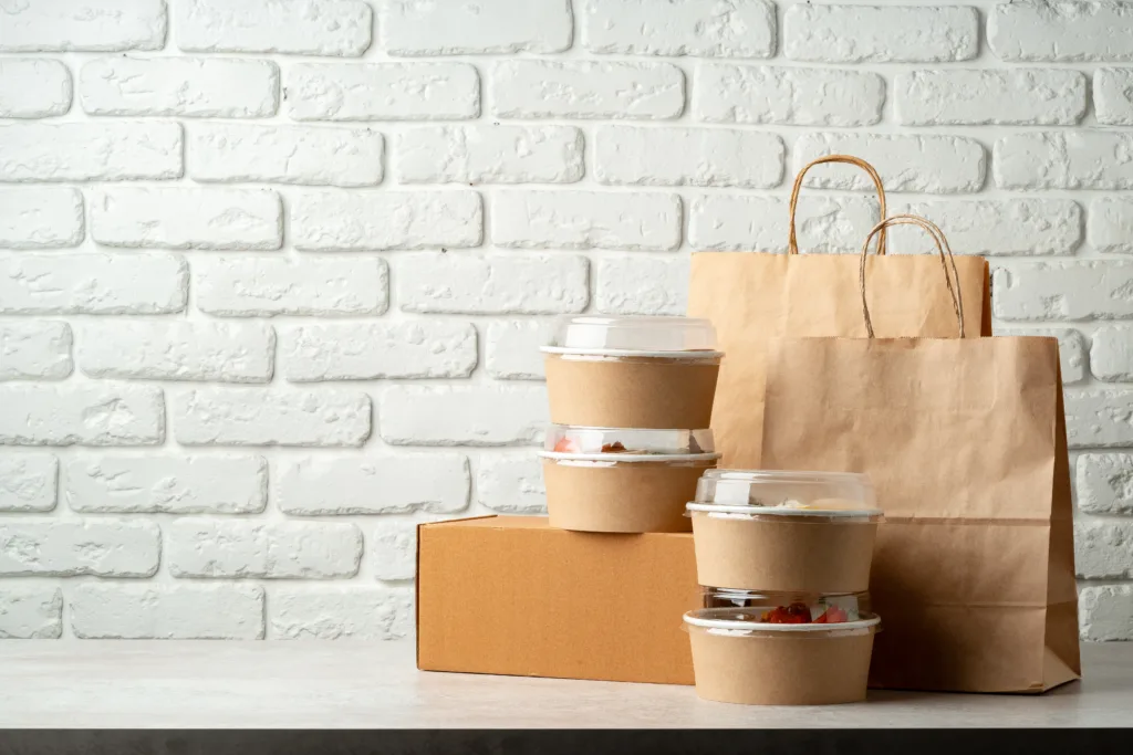 Take out food in boxes and craft bag against white brick background