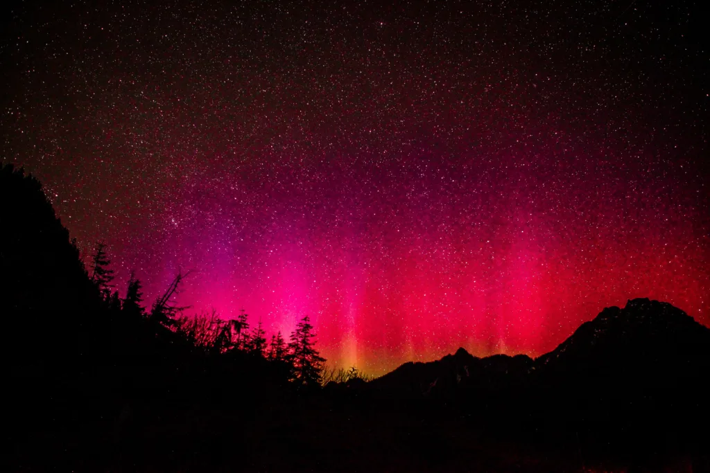 Vivid magenta and red hue northern light sky with spectacular starry display over mountain and valley silhouette