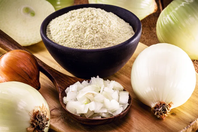 wooden spoon with sliced onion and crushed into pieces to be used as seasoning, with powdered onion in the background, rustic kitchen