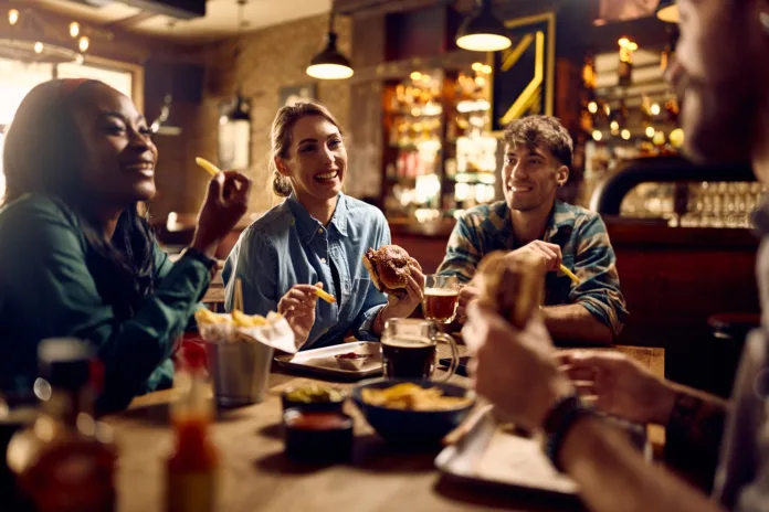 Young happy woman and her friends talking while eating in a pub.