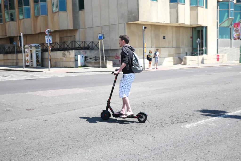 Brighton, UK - June 14, 2021: A young man on an electric scooter crosses the road