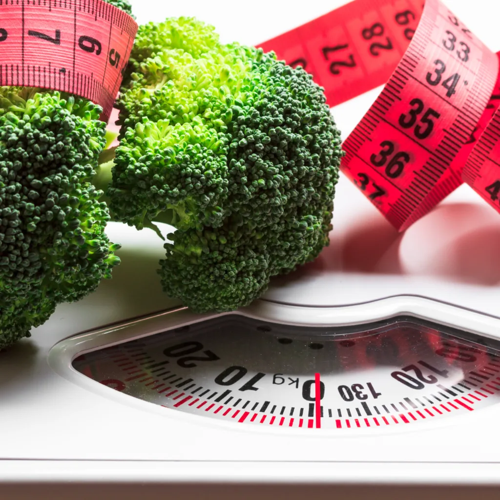 Dieting healthy eating slim down weight control concept. Closeup green broccoli with measuring tape on white scales