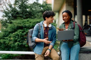 Happy African American student and her friend surfing the net on laptop at campus.