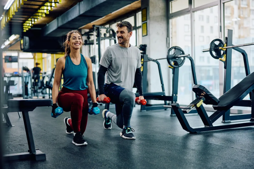 Happy athletic couple having weight training in lunge position at health club. Copy space.