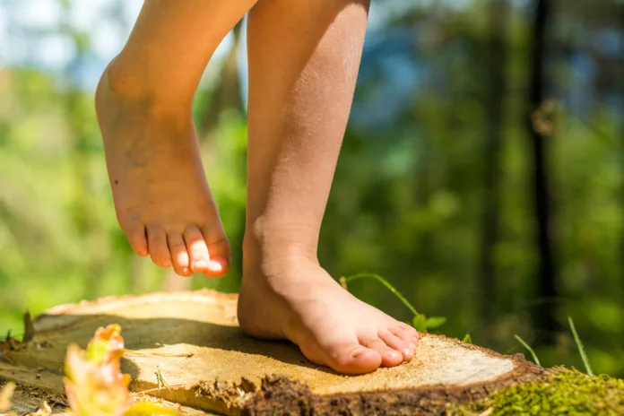 Happy barefoot girl child standing on tree trunk in the woods.