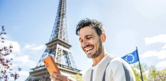 Happy tourist booking hotel with smart mobile phone device in Paris, France - Handsome young man using date app with smartphone - Travel, technology and youth concept