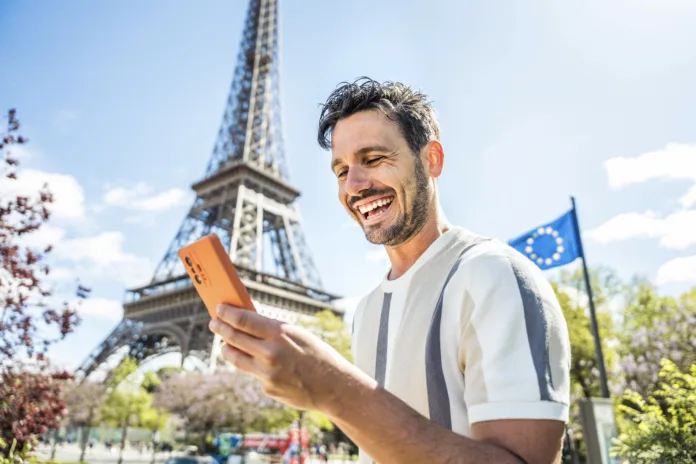 Happy tourist booking hotel with smart mobile phone device in Paris, France - Handsome young man using date app with smartphone - Travel, technology and youth concept