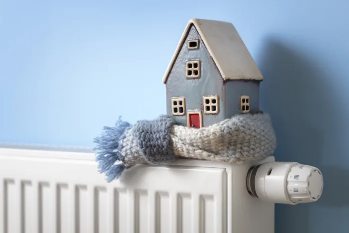 House model wrapped in scarf on radiator home winter heating and insulation background fuel and energy crisis concept