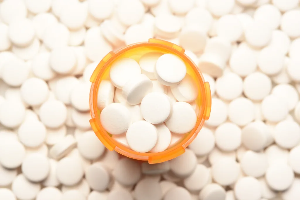 Opioid Crisis Concept: High angle view of a prescription bottled filled with pills surrounded by more of the same tablets.