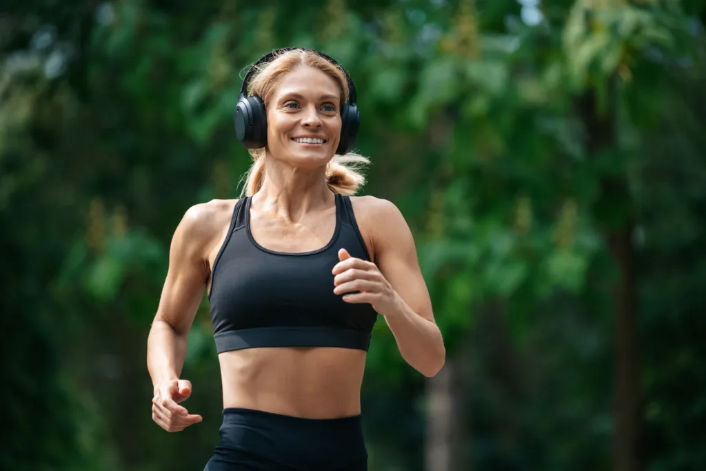 Road to health. Running in nature. Athletic strong blonde runner woman in headphones jogging in park.