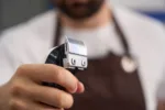 Selective focus photo of electric hair clipper in hand of a dedicated barber wearing an apron