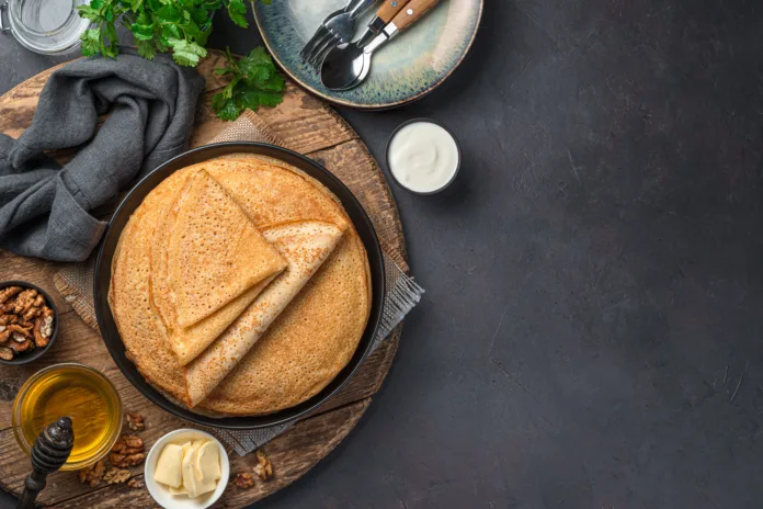 Stack pancakes on a dark background with honey, sour cream and nuts. Russian blini. Mardi Gras. Top view, copy space.