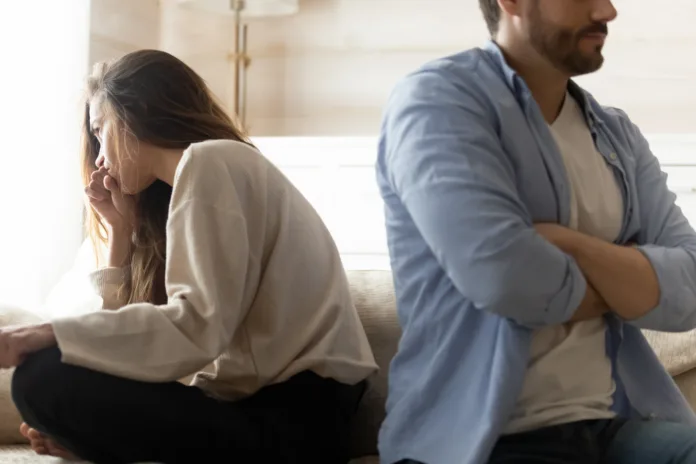 Stressed young married couple sitting separately on different sides of sofa, ignoring each other after quarrel. Offended spouses do not talk communicate, feeling depressed disappointed after argue.