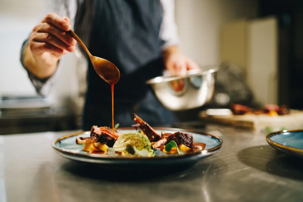 The chef pouring special sauce on pork ribs in the kitchen