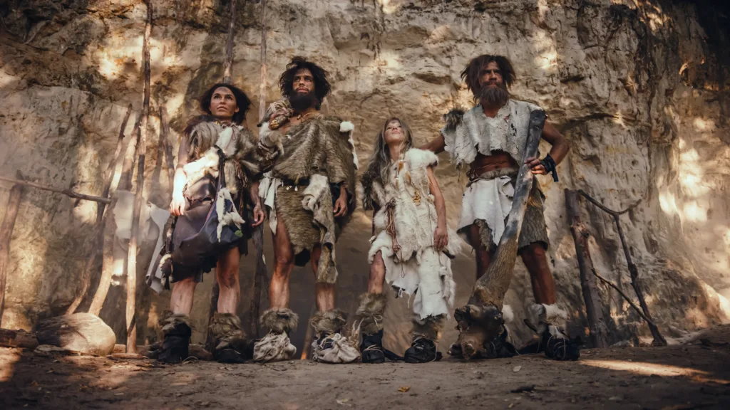 Tribe of Four Hunter-Gatherers Wearing Animal Skin Holding Stone Tipped Tools, Pose at the Entrance of their Cave. Portrait of Two Grown Male and Two Female Neanderthals and their Way of Living