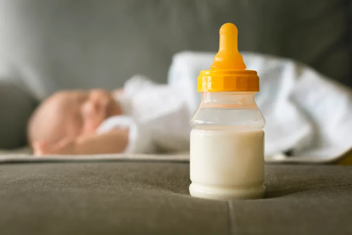 A bottle of milk displayed infront of a sleeping baby.