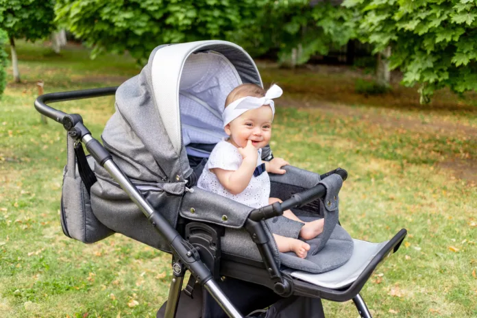 a small child a girl of 7 months sits in a stroller in the summer in a white dress and looks at the camera