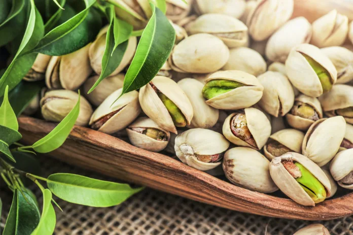 Bowl with pistachios nut on a wooden table with green leaves. Pistachio nuts detail..