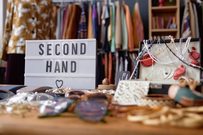 Close up on sign with inscription Second Hand and jewelry case with vintage accessories at thrift store checkout, copy space