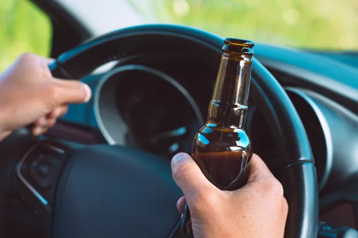 Closeup of drunk driver hands on the steering wheel with a bottle of beer. Driving under alcohol influence. High quality photo