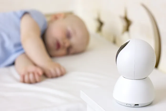 Cute little baby boy sleeping on bed at home with baby monitor camera. Selective focus. Child daytime sleeping. Modern technology.