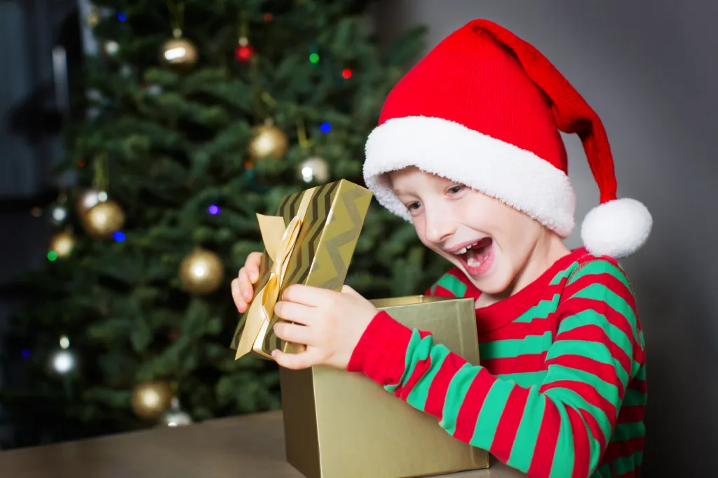 excited little boy opening christmas present at home by the tree being happy and enjoying cozy time