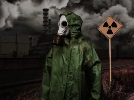 Man in gas mask and cloak of chemical protection on abandoned road in front of Nuclear station. Nuclear pollution concept