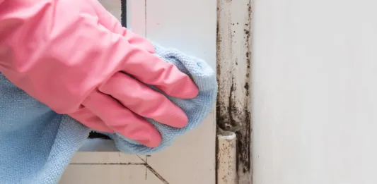 Mold in the window corner. Hand in rubber protective glove with microfiber cloth trying remove it.