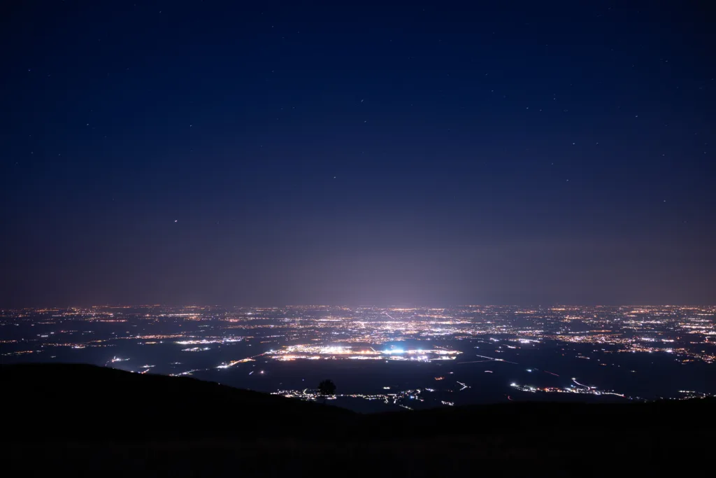 panoramic view on the cities in landscape in the western area of Friuli Venezia Giulia region, partially covered by thing fog, while looking at the clear starry blue sky at night. Highlands of Piancavallo, Italy