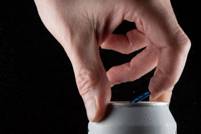 A man's hand opening a soda can on a black background and showing the splash when opening the can.